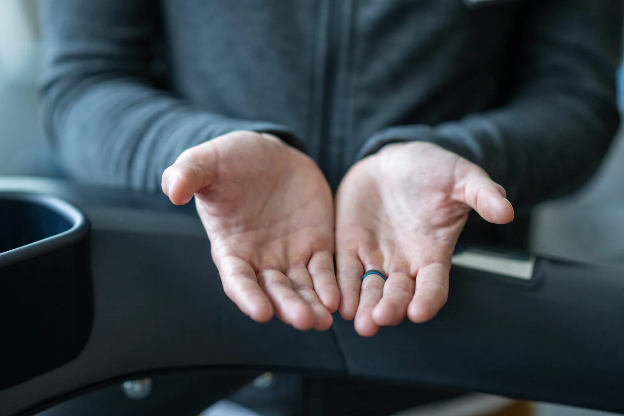 Close-up of two open hands, palms up, with a black and blue ring on one finger, against a blurred background.