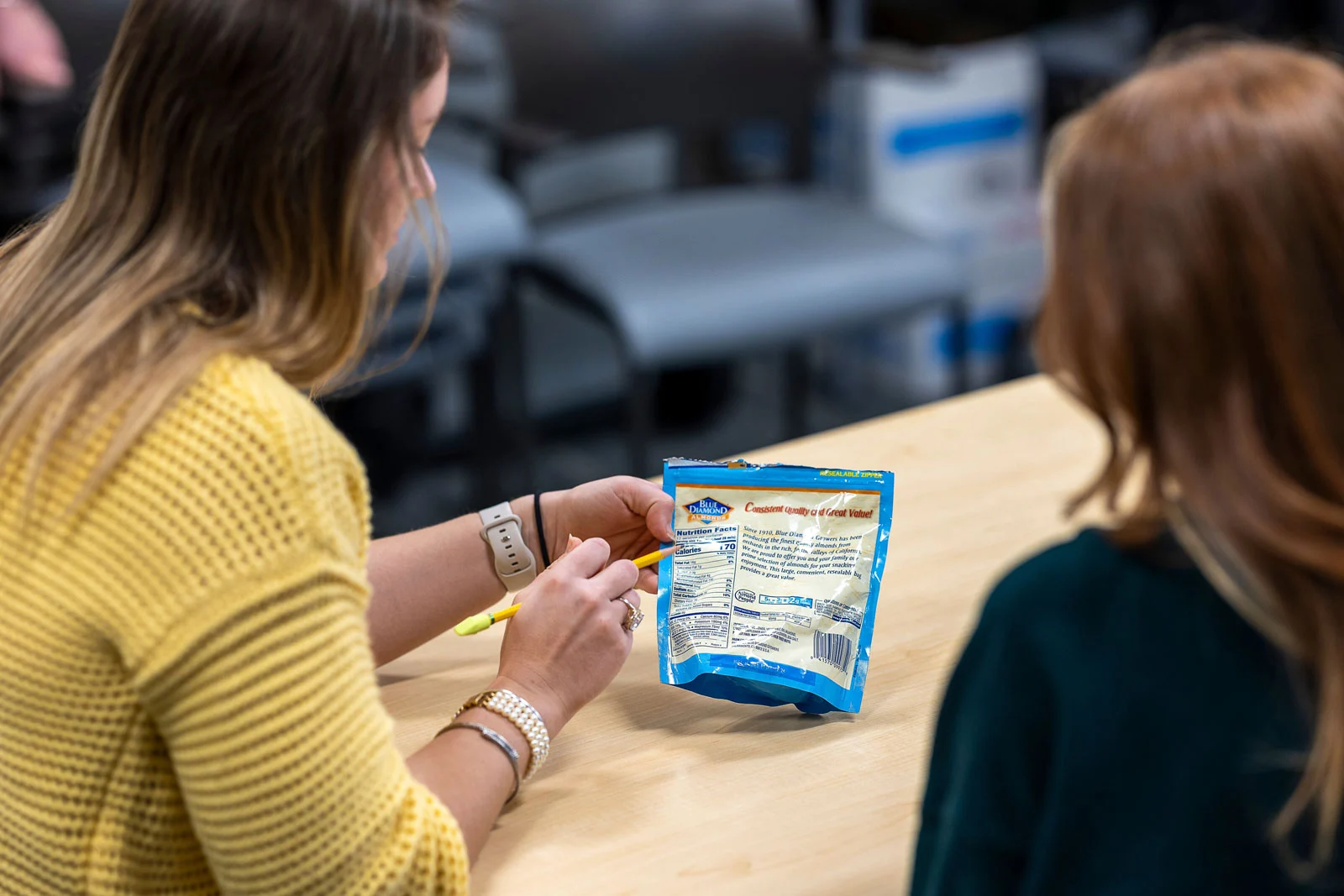 A person in a yellow sweater holds a blue Blue Diamond almond package, pointing at the nutrition facts with a yellow highlighter.