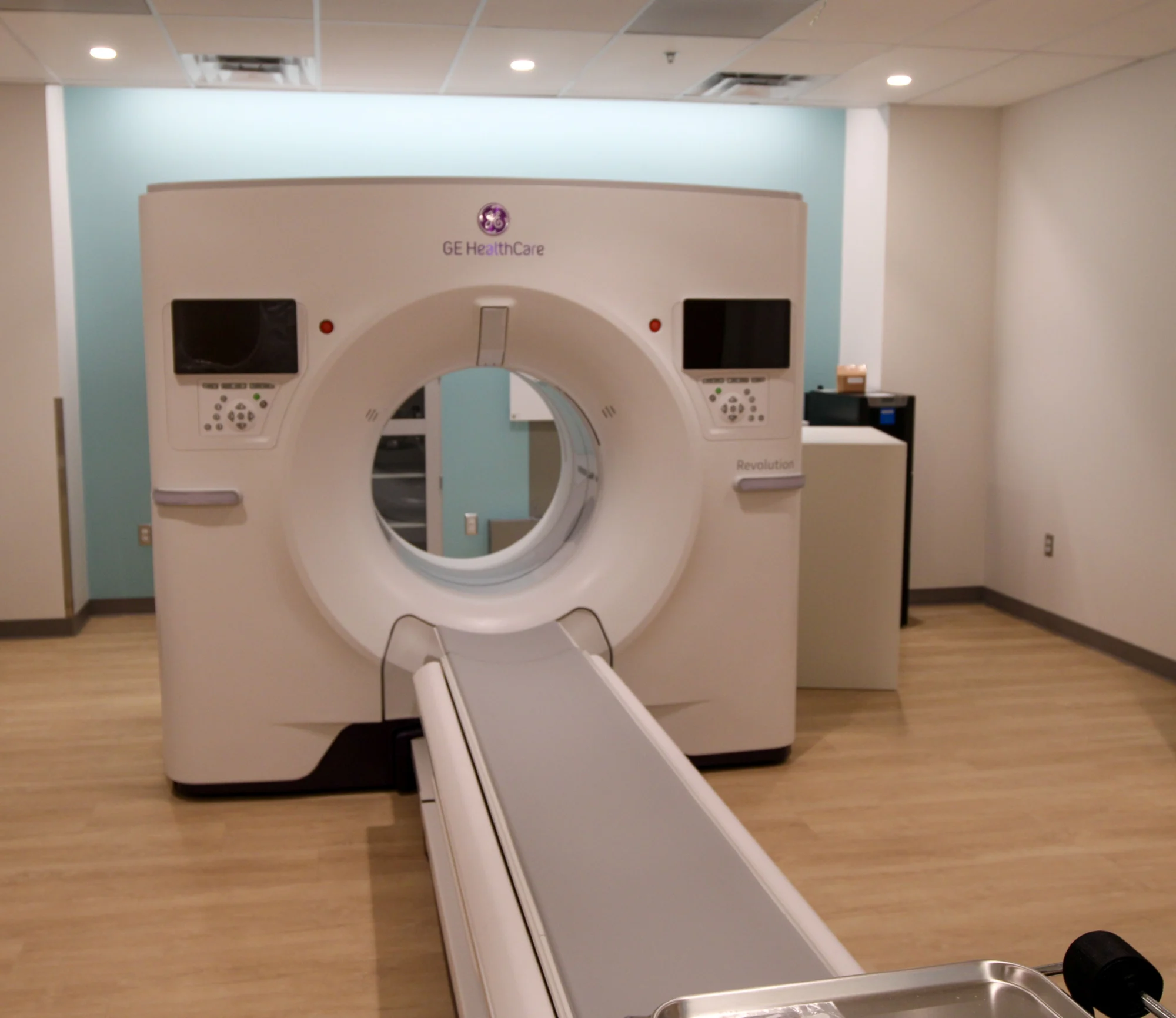 A GE HealthCare Revolution CT scanner with a patient table in a clean, modern medical room with white and light blue walls.