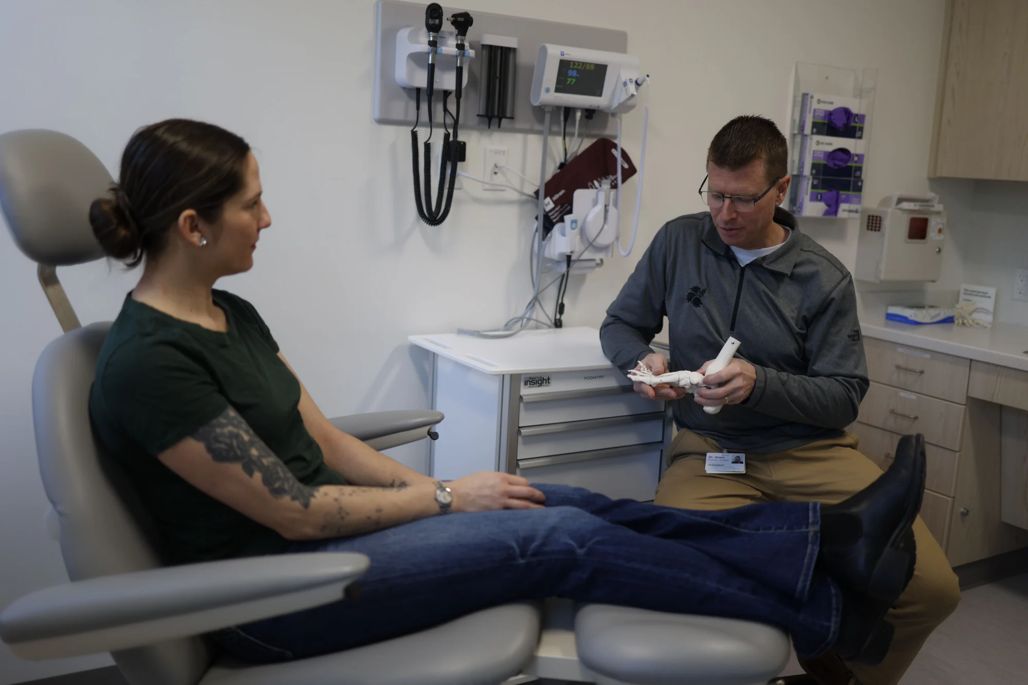 A doctor uses a foot model to explain to a patient in a medical examination room.