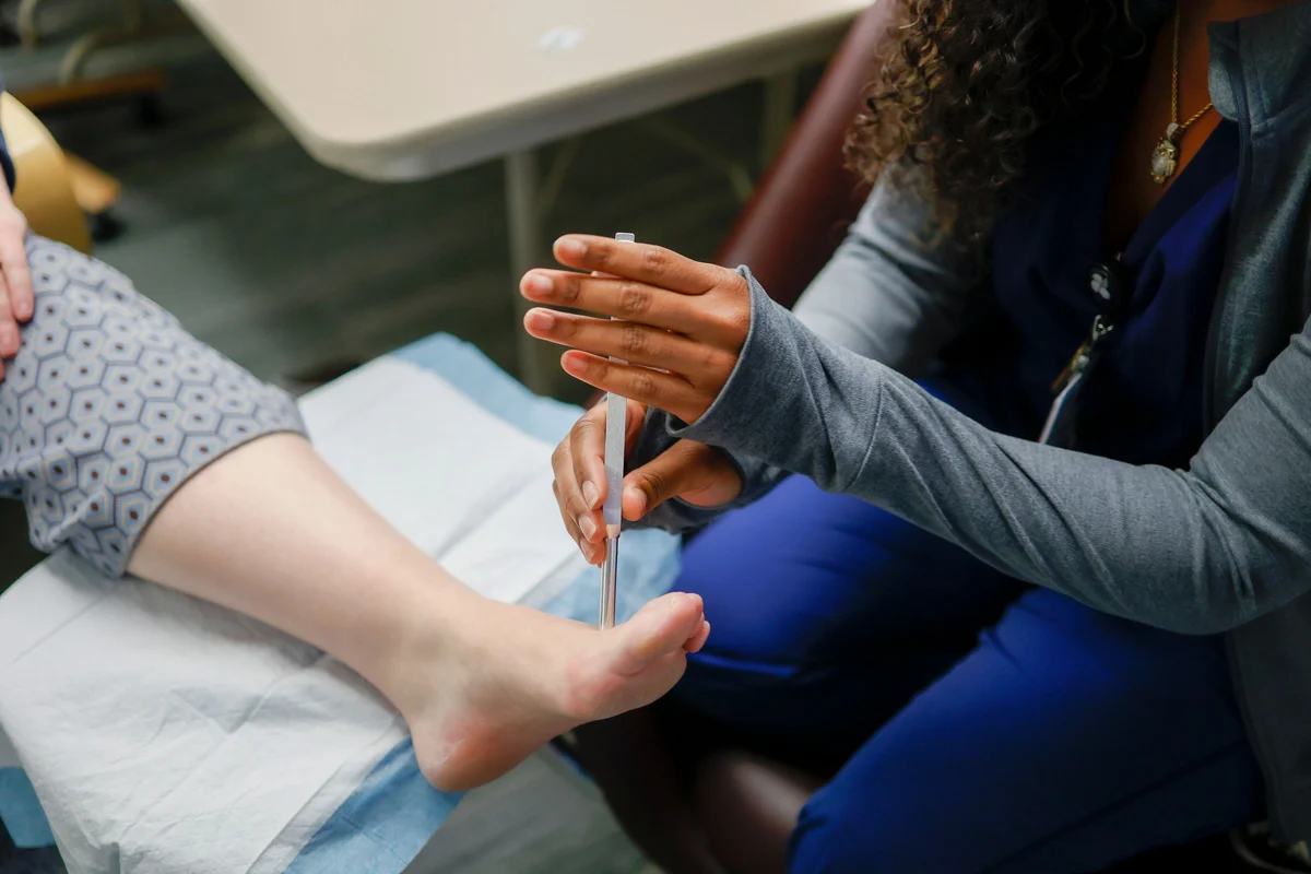 Close-up of a medical professional's hands holding a monofilament tool to test the sensation on a patient's foot.
