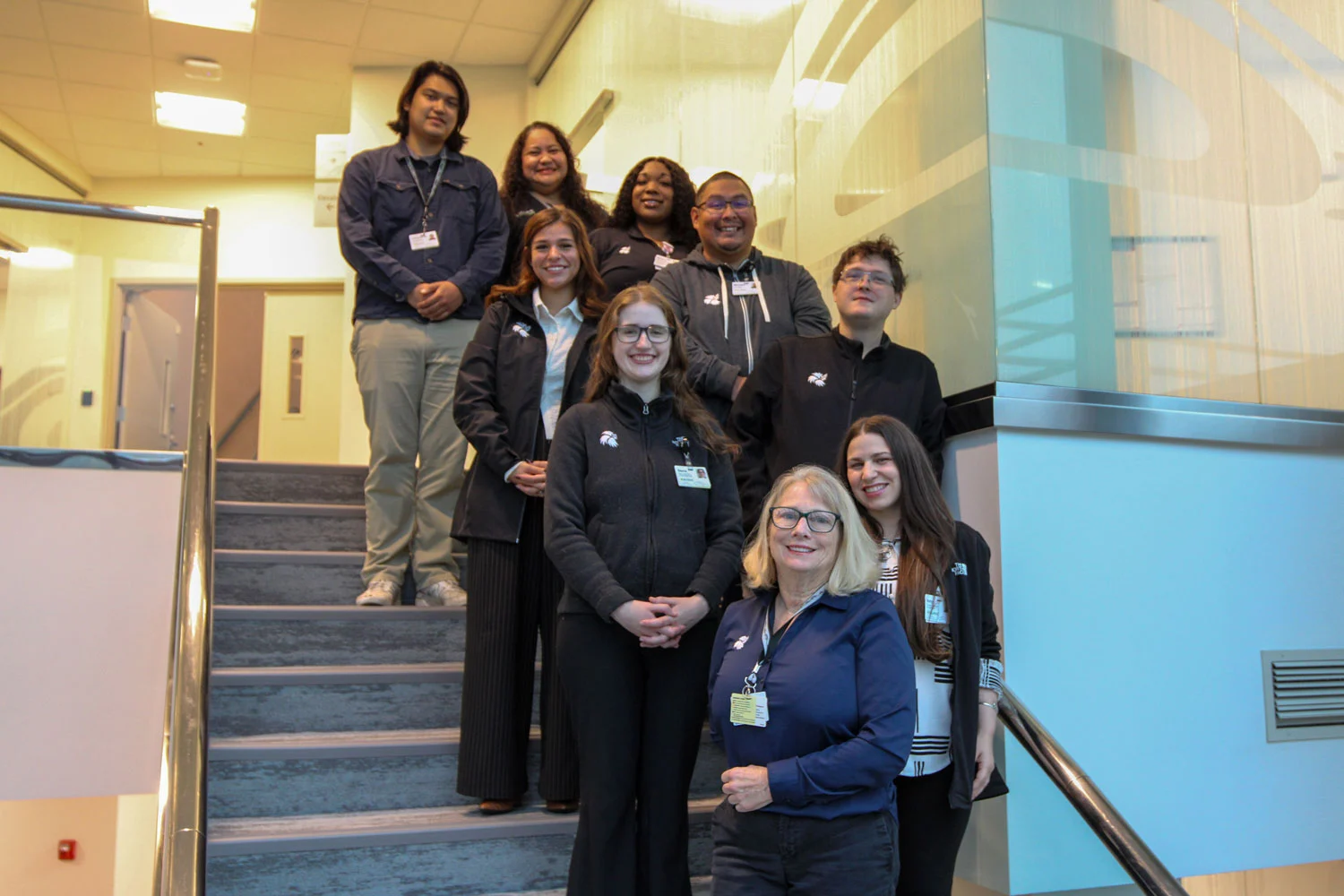 Ten people, men and women, smiling and posing on a staircase indoors.